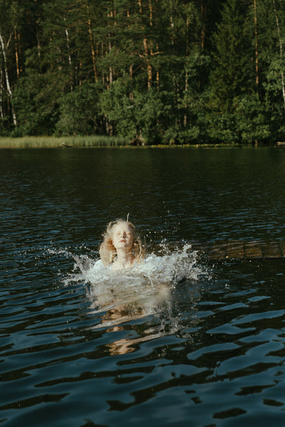 A swimmer breaking the surface of a still, tree lined forest lake