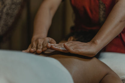 A therapist working warm oil across a back in a dark room, the Ayurvedic bodywork at the heart of the treatment menu