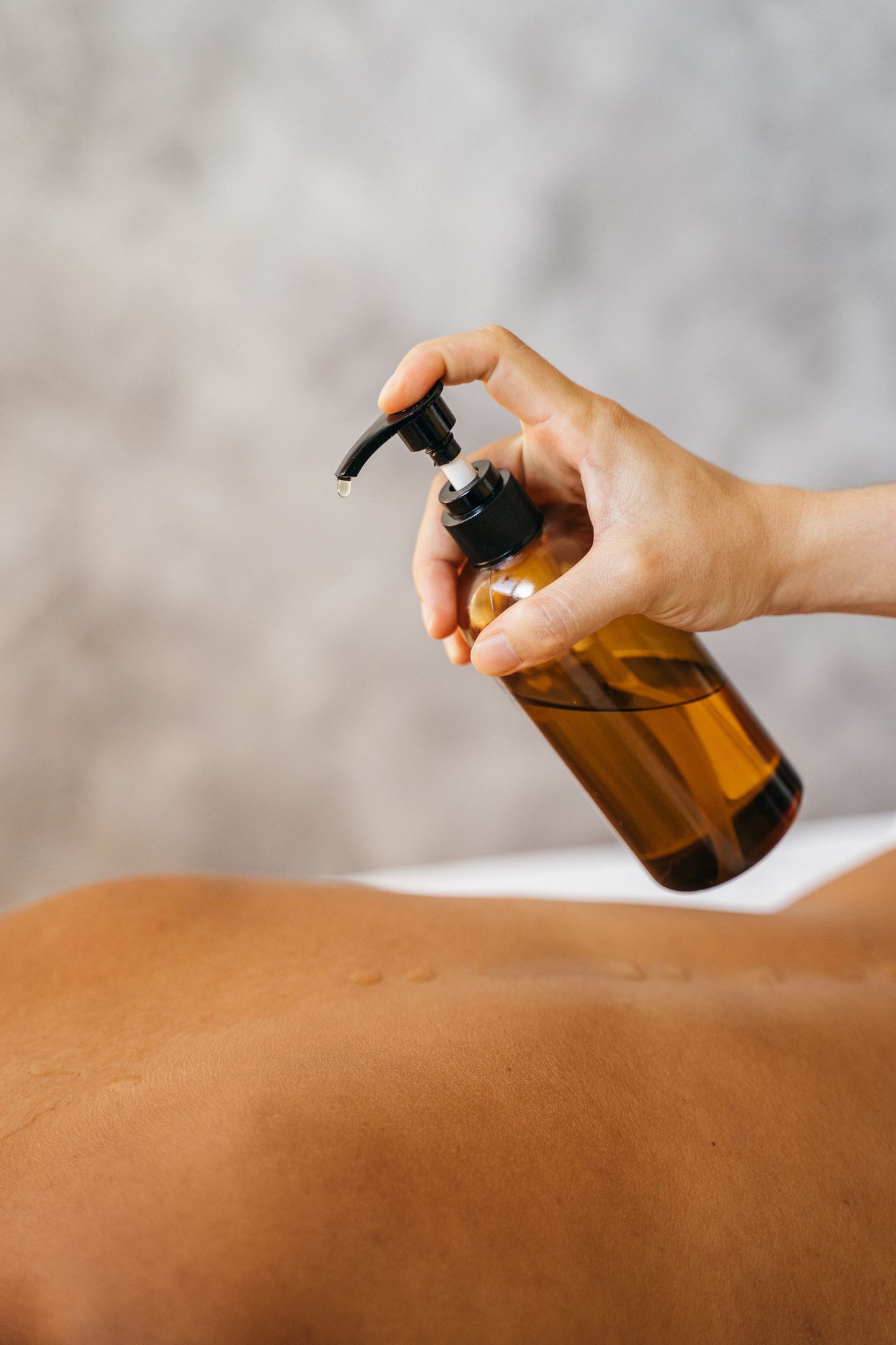 A therapist's hand pressing warm oil onto a client's back during a massage.