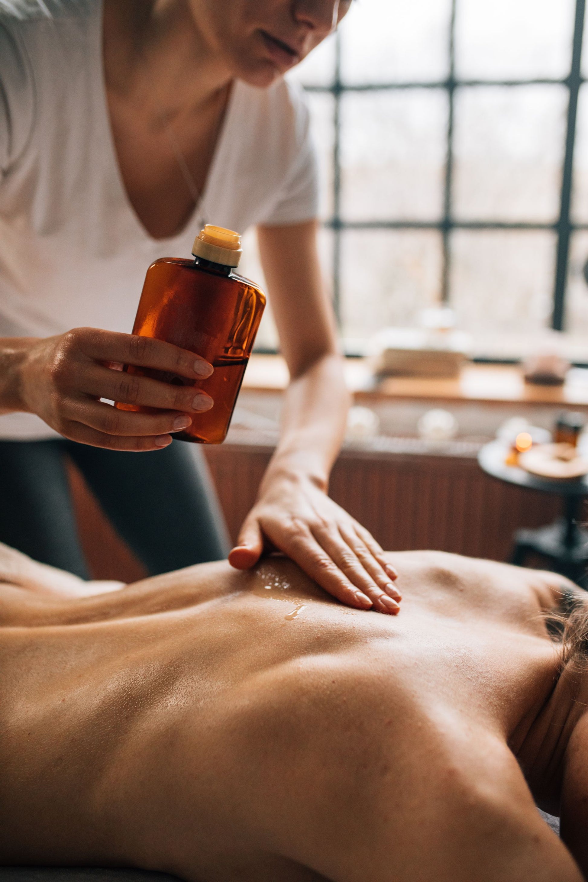 A therapist pouring warm oil from an amber bottle before a back massage.
