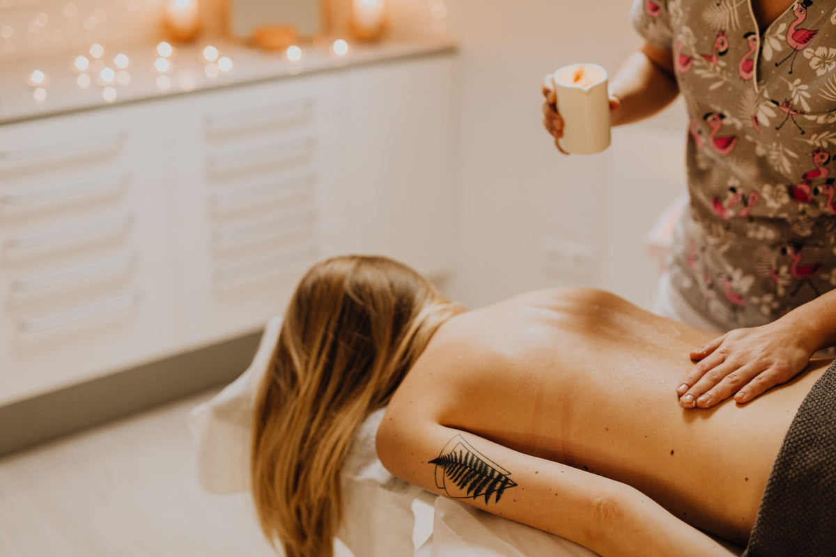 A therapist's hands working warm oil into a guest's back by candlelight, evoking a silver fir massage at the spa in Megève
