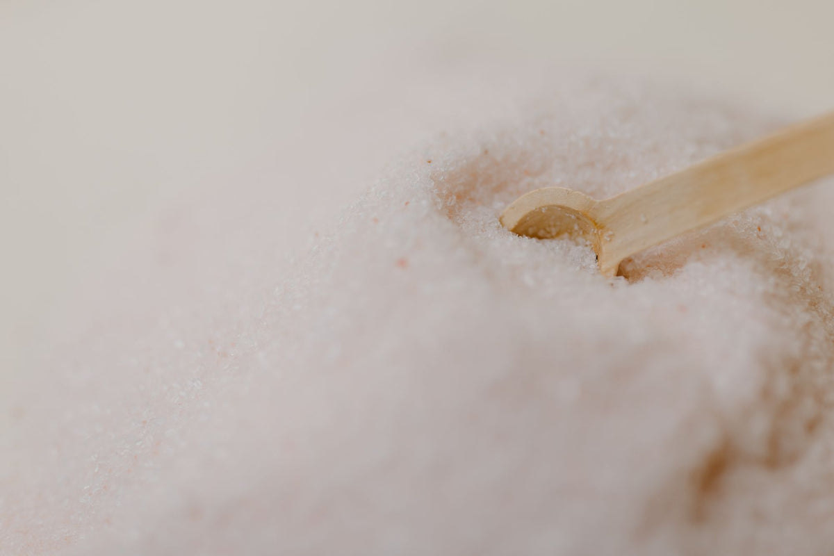 A wooden spoon rests in coarse pink salt, close and textural, echoing a Himalayan salt relaxation room