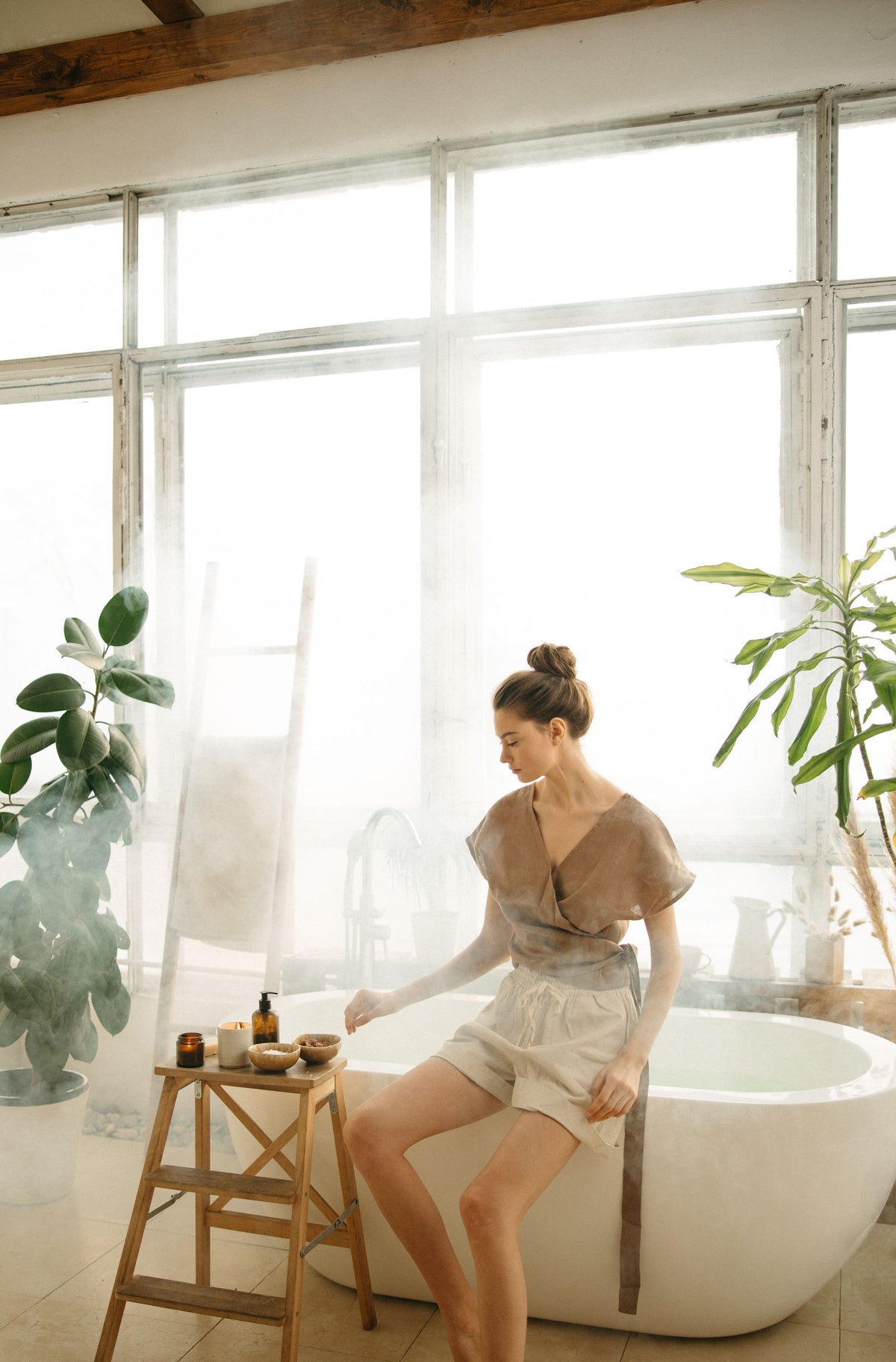 A guest resting with eyes closed beside a freestanding bath in a bright, plant filled room, evoking the quiet of a treatment at the spa