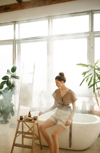 A guest resting with eyes closed beside a freestanding bath in a bright, plant filled room, evoking the quiet of a treatment at the spa