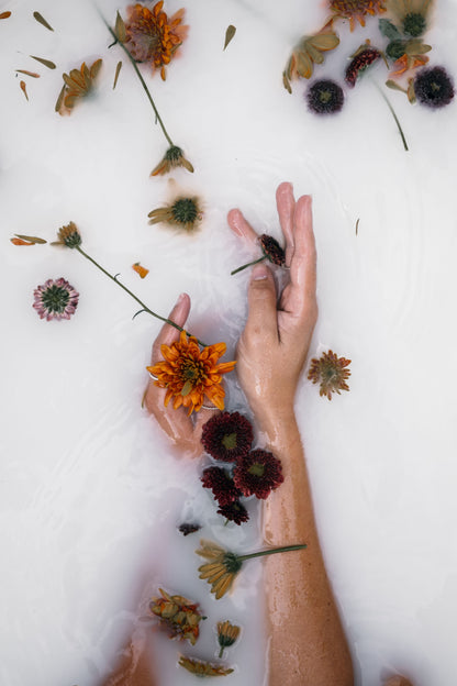 A hand setting botanicals into a bath of clouded water, The Meadow Spa at Thyme, Southrop
