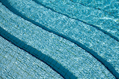 Sunlit ripples over blue tiled swimming pool water