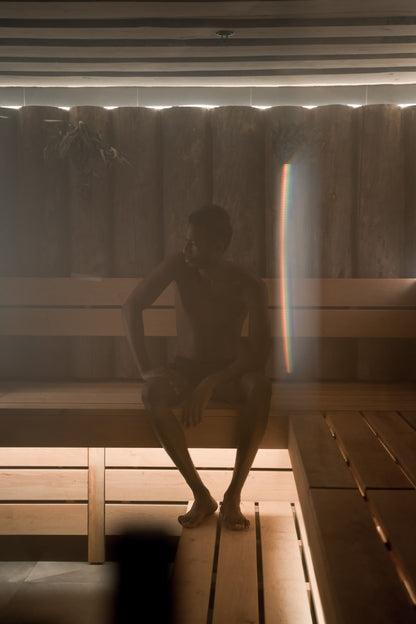 A figure silhouetted in the warm glow of a wood panelled sauna, evoking the spa's private saunas and steam rooms