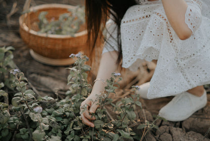 A woman in a white dress cuts herbs beside a wicker basket, an evocative image for the herb picking walk that opens the signature massage at The Newt in Somerset